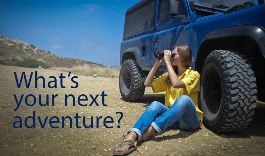 Blue Jeep with woman sitting on ground with binoculars next adventure
